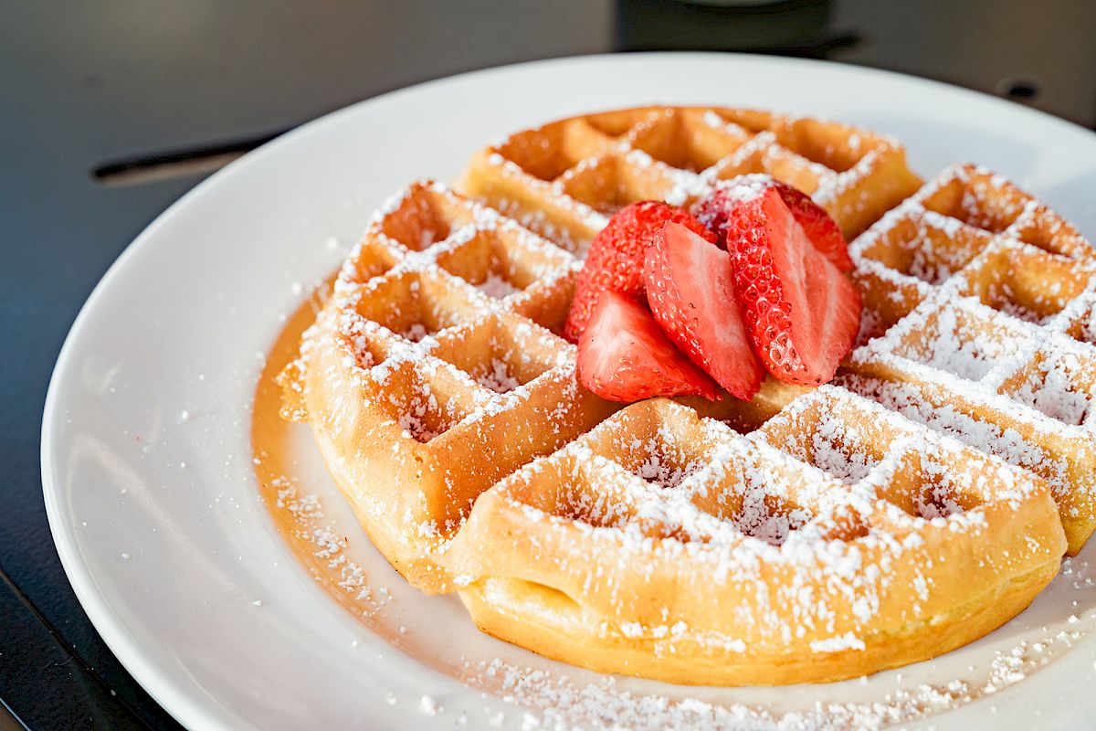 A plate of waffles topped with powdered sugar and fresh strawberry slices.